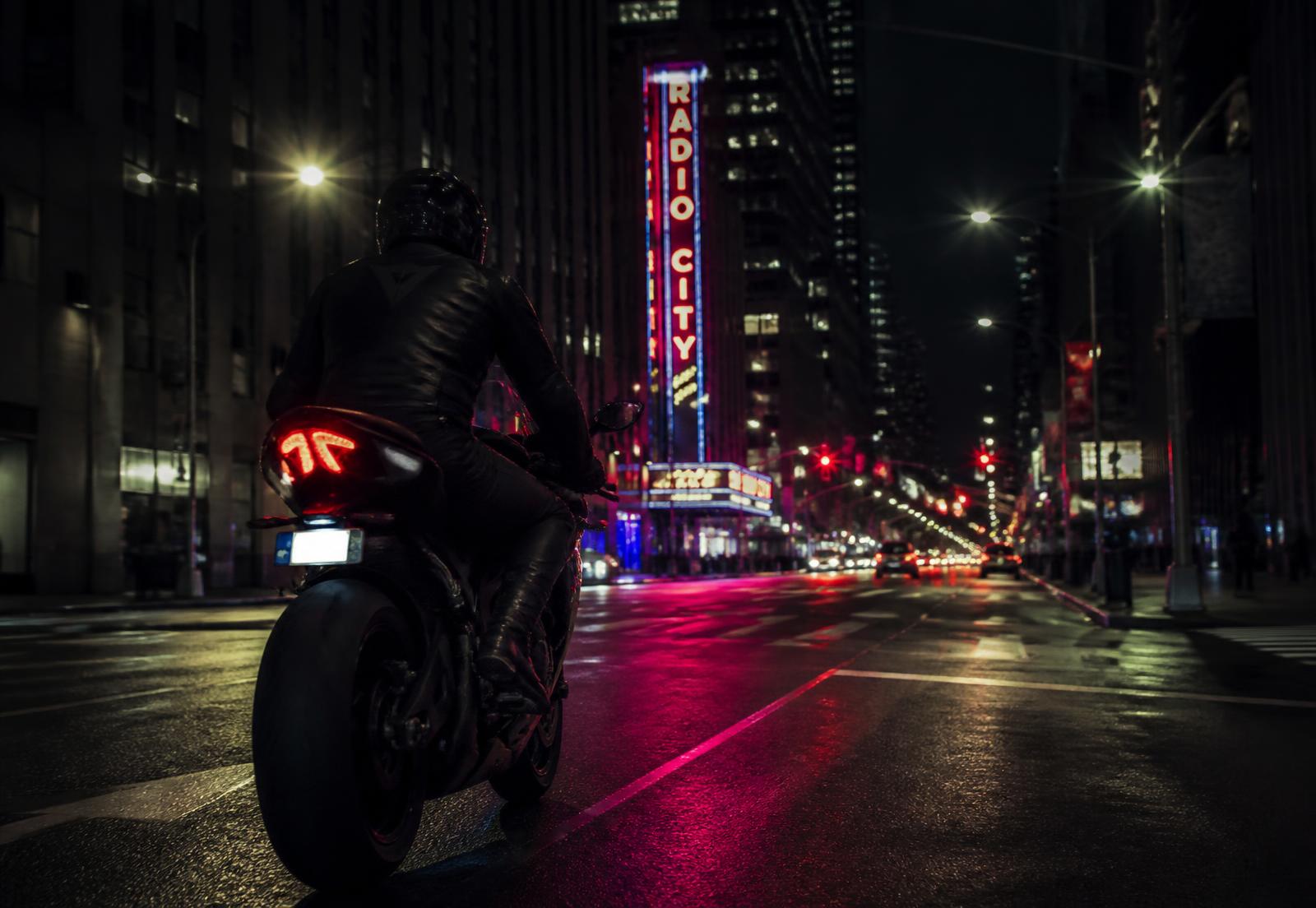 Motociclista em avenida urbana à noite com reflexos de luzes no asfalto